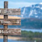 wooden signs that say Follow Your Heart with mountain and lake in the background