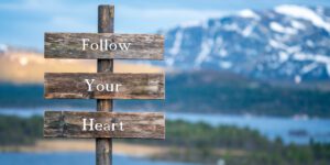 wooden signs that say Follow Your Heart with mountain and lake in the background